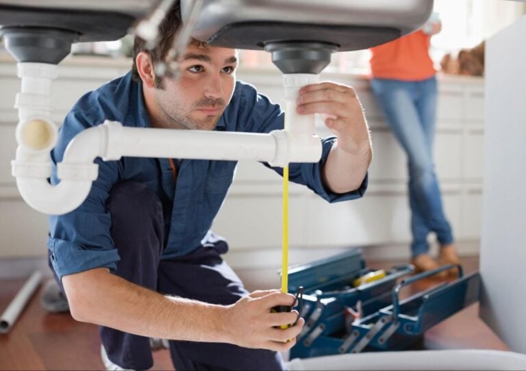 A contractor inspects pipes under a kitchen sink, with open toolboxes nearby—showcasing Hook Agency’s plumbing web expertise.