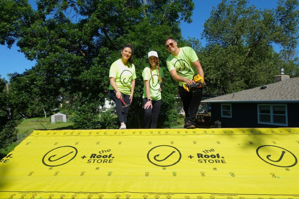 Three team members in neon green shirts stand on branded yellow roofing underlayment, representing Hook Agency’s expertise.