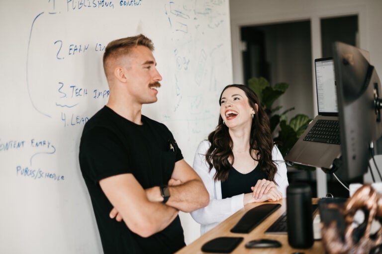 Industry professionals collaborate at a desk before a note-filled whiteboard in Hook Agency’s modern office; smiling, engaged.