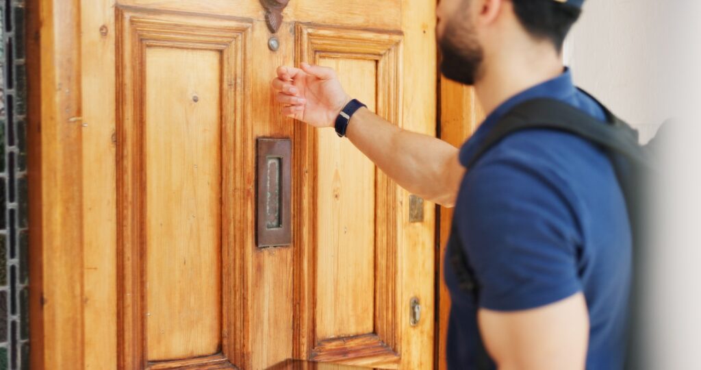 A roofing sales professional in a blue shirt and backpack prepares to knock on a wooden front door, ready to apply proven sales strategies.