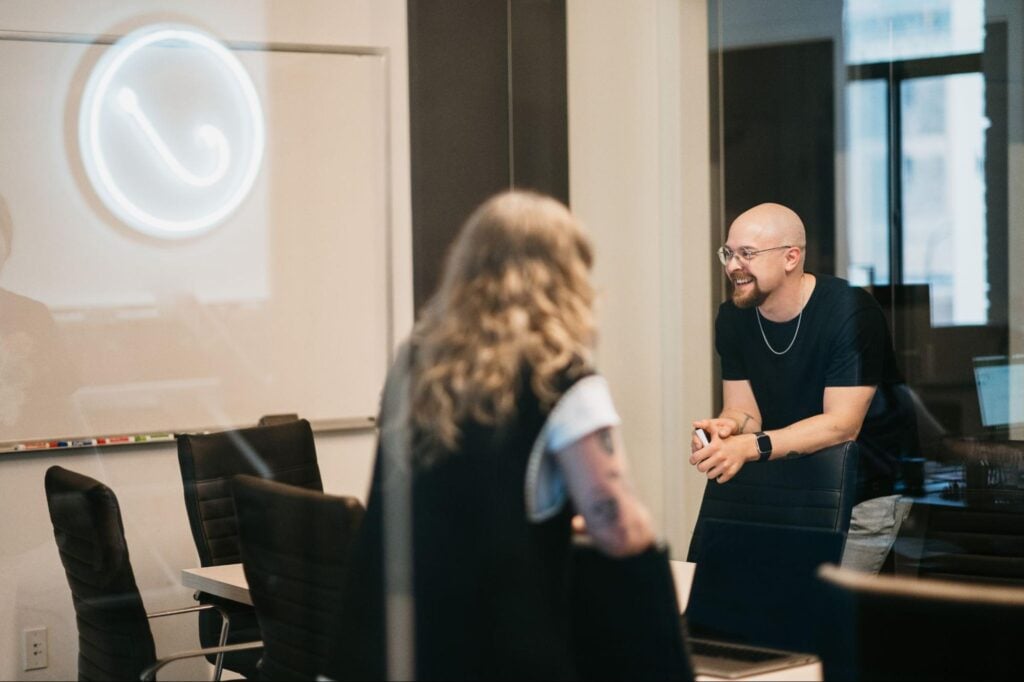 A man and woman discuss Google strategy in a modern office at Hook Agency, with a whiteboard and chairs in the background.
