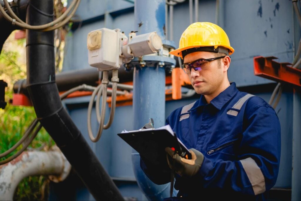 Industrial worker in PPE inspects equipment and records data at an outdoor facility serving homeowners—Hook Agency project in action.