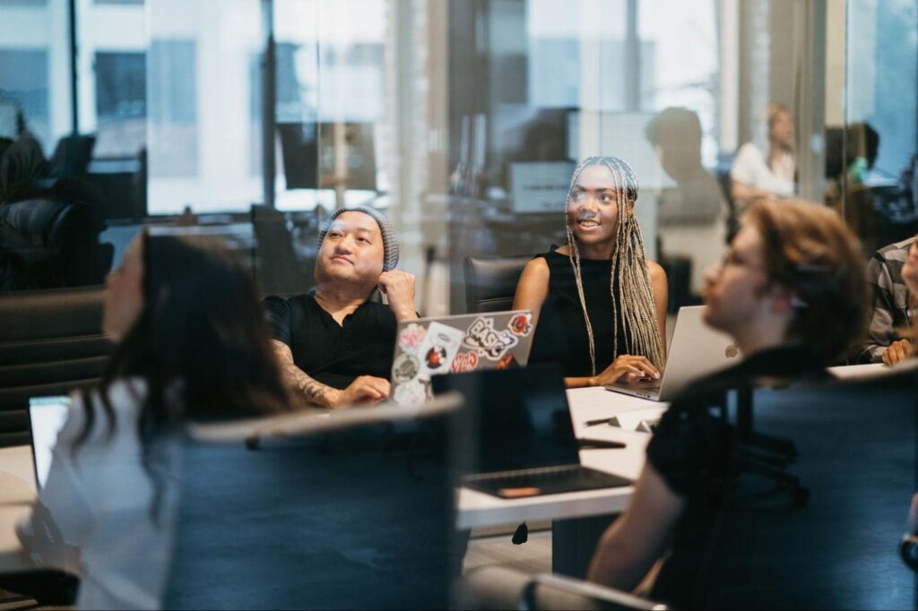 Team of four at conference table strategizing contractor marketing on a budget, laptops open, busy office visible through large windows.