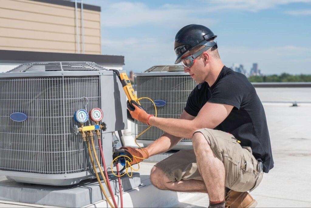 Technician in safety gear inspects rooftop HVAC unit with tools, city skyline behind—protecting margins by preventing profit killers.