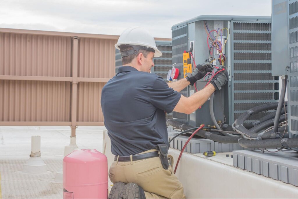 Technician in hard hat and gloves services rooftop HVAC unit with tools; pink refrigerant tank nearby—ideal for HVAC marketing.