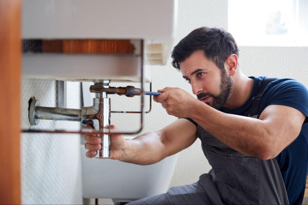 Professional plumber in overalls repairs a bathroom sink pipe with a wrench, focused on expertly tightening fittings.