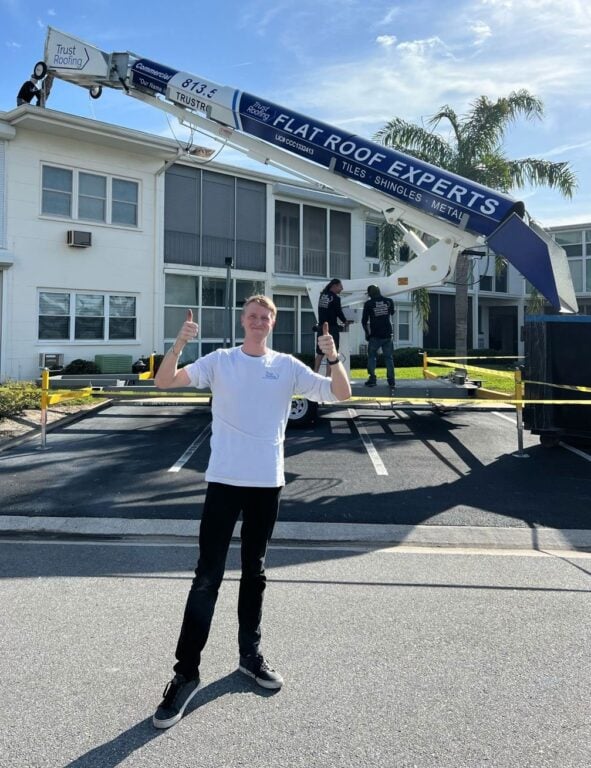 A person in a white shirt (Robin Scherer, owner of Trust Roofing) is smiling and giving a thumbs up in front of a large piece of roofing equipment labeled "Flat Roof Experts." It's part of an impressive roofing marketing case study for Trust Roofing by Hook Agency. Two other people work on the machine, with a building and palm trees visible in the background.