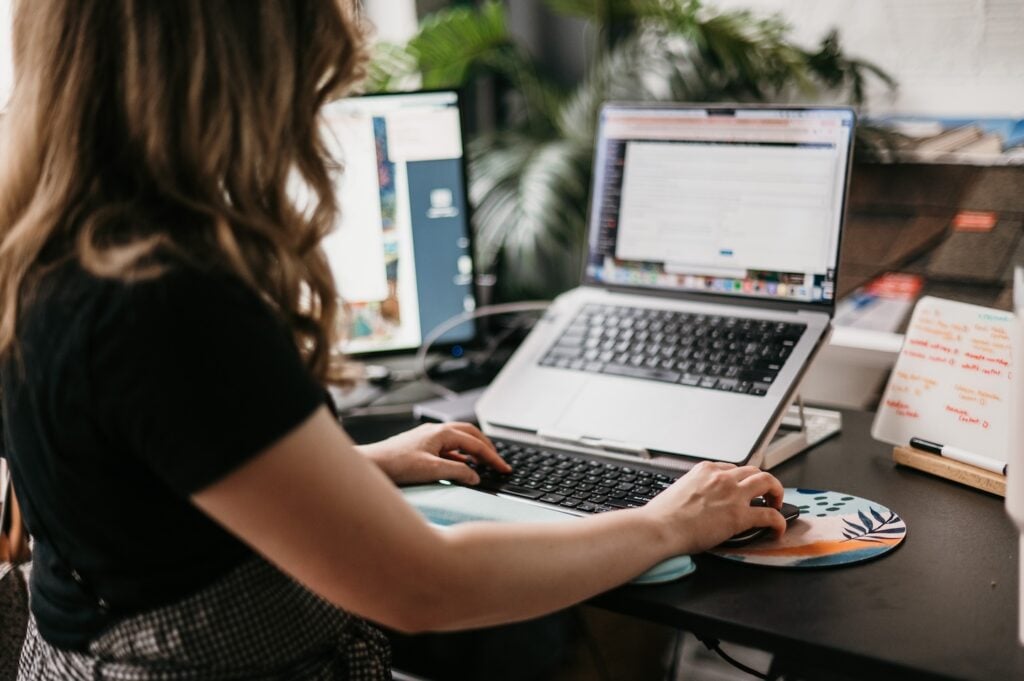 Hook Agency team member develops contractor marketing strategies at a desk with laptop, monitor, whiteboard notes, and plants.