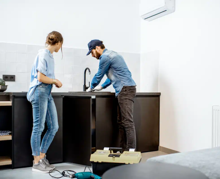On Hook Agency's website, a man and woman work efficiently in a kitchen. The man, equipped with a cap and gloves, inspects beneath the sink like an expert electrician. The woman, dressed in a light blue shirt and jeans, attentively observes the process. Nearby, a toolbox and equipment suggest tools vital to their marketing services.