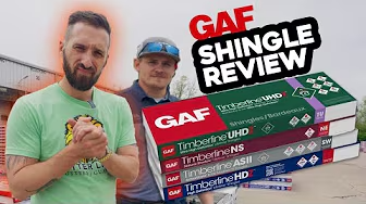 Two men stand outside by a building with four stacked GAF Timberline shingle packs. "GAF Shingle Review" appears above as text.