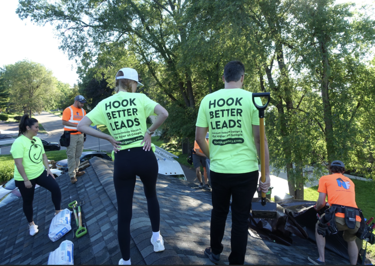 On Hook Agency's website, a vibrant image depicts a team energetically working on a roof. Two members in fluorescent green shirts prominently showcase the slogan "HOOK BETTER LEADS," symbolizing our cutting-edge roofing website design solutions. The scene, set against a clear blue sky with visible trees and streets, highlights hands-on expertise and innovation in lead generation for roofers.