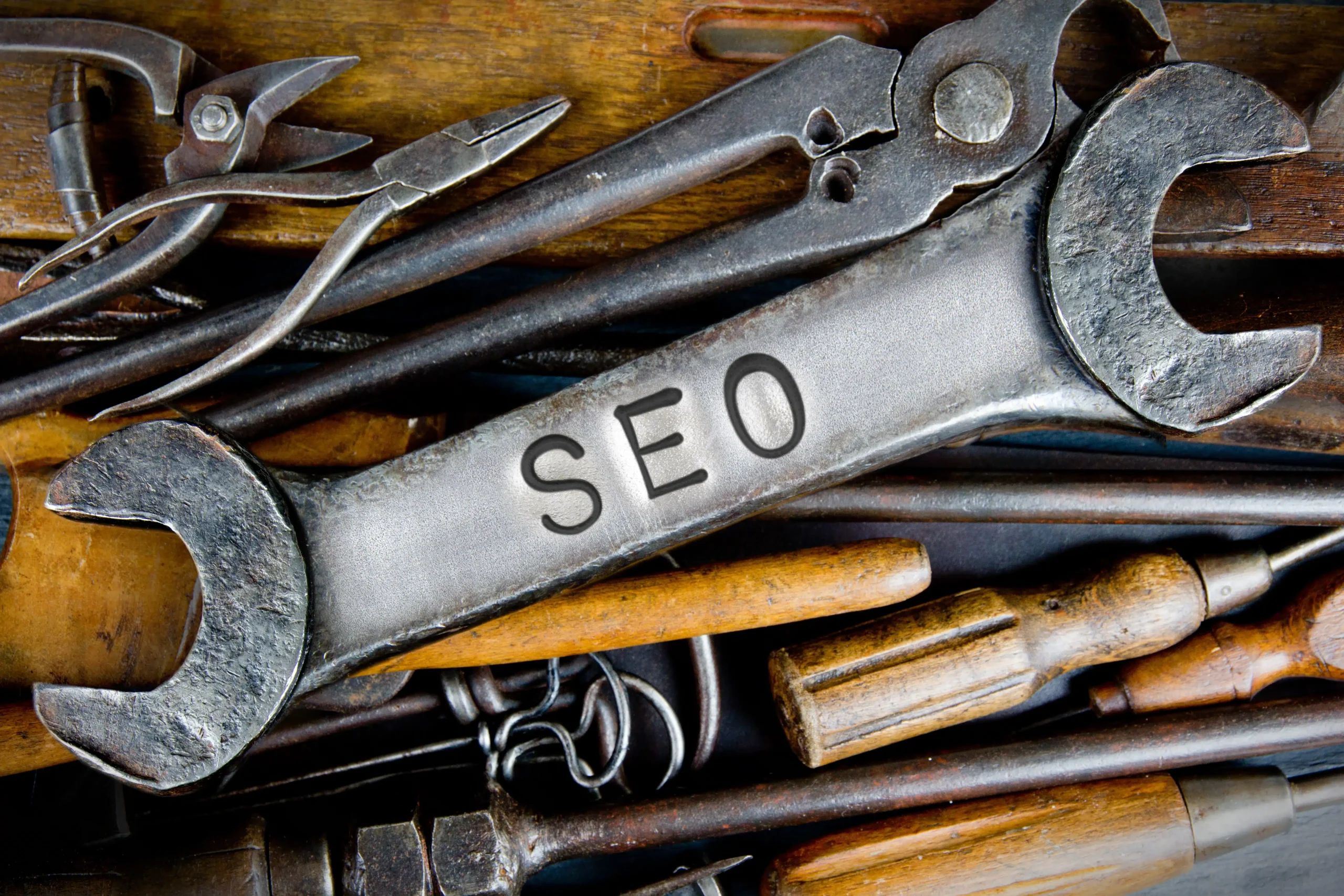 A variety of hand tools, including a wrench engraved with "SEO," are displayed on a wooden surface. This image represents SEO as an essential toolset for enhancing and constructing an online presence.