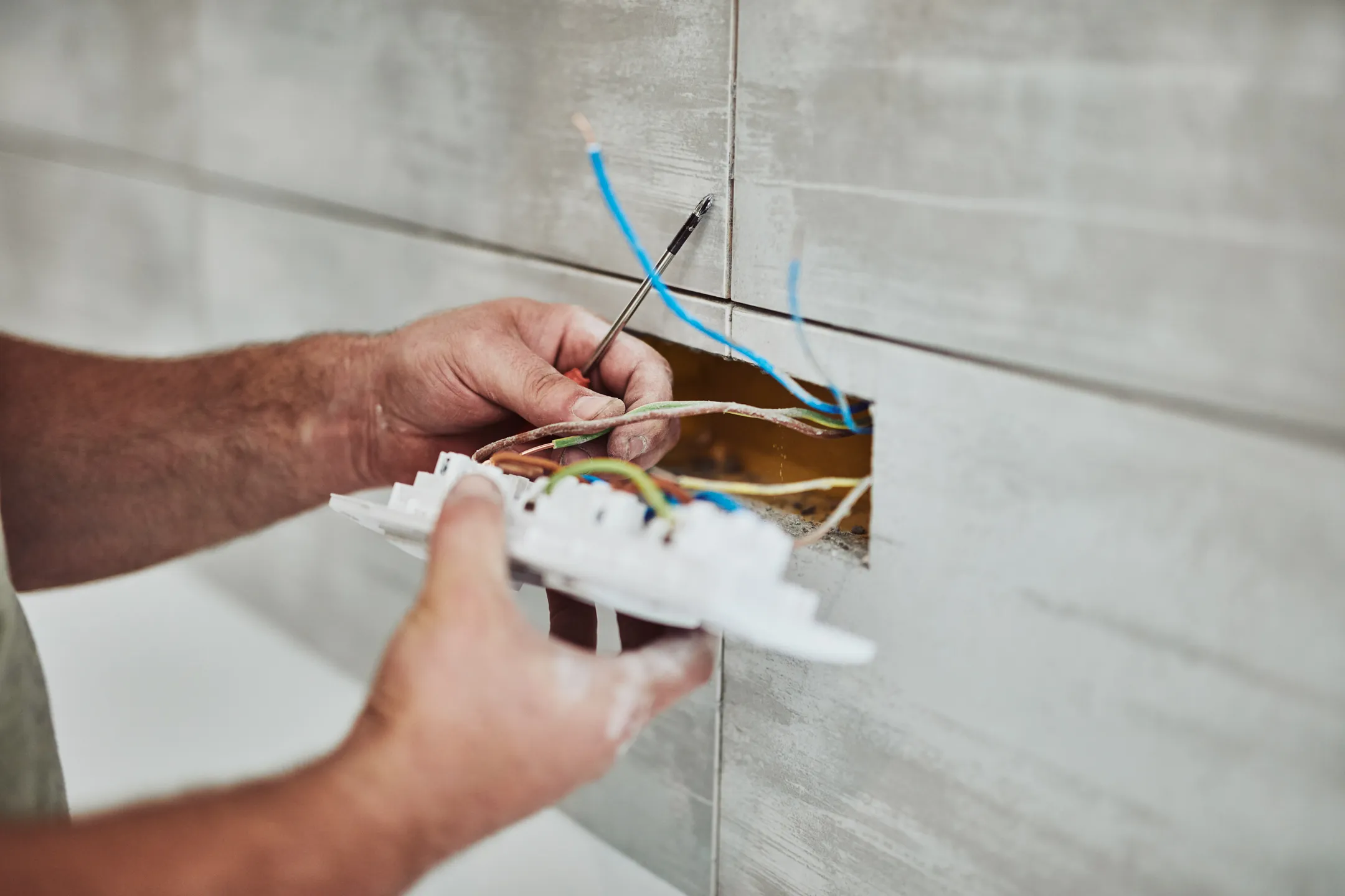 An electrician expertly installs a light switch, precisely connecting wires with a screwdriver. This seamless execution demonstrates superior craftsmanship—a prime example of exceptional electrician marketing at Hook Agency.