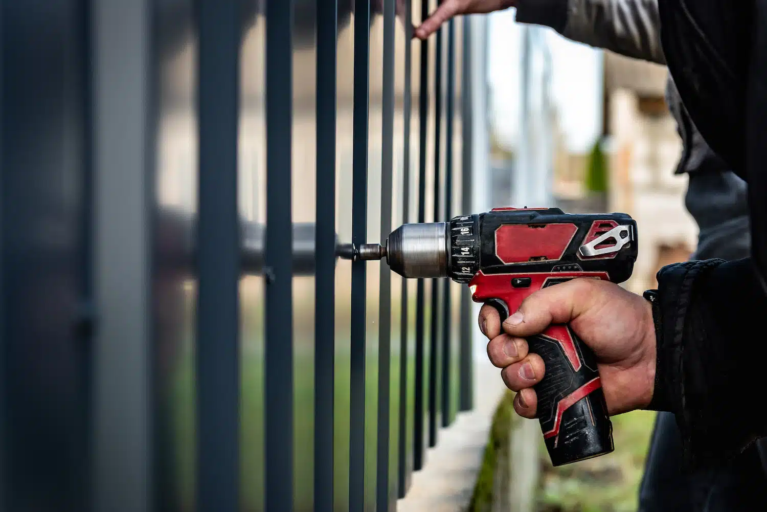 On Hook Agency's website, a professional from a fencing company skillfully uses a black and red power drill to secure a metal component onto a fence. While another hand stabilizes the structure, this outdoor scene epitomizes precision and expertise in construction or repair work.