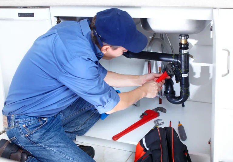 A skilled plumber in a blue shirt and cap efficiently repairs kitchen sink plumbing issues, demonstrating precision and expertise. His organized toolkit by his side signifies the meticulous approach shared by Hook Agency's effective SEO strategies for plumbing businesses.